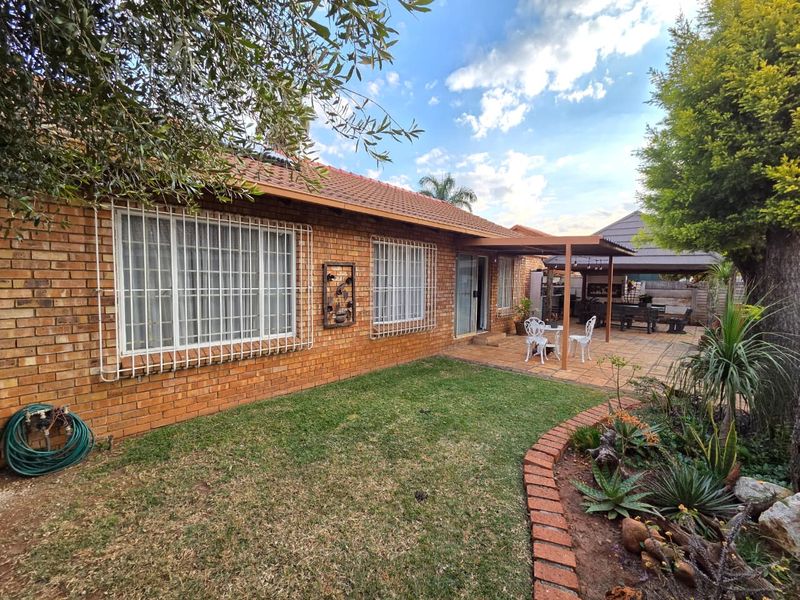 Rear view of the townhouse featuring a face-brick facade, a paved covered patio area, and a well-maintained garden with established landscaping.