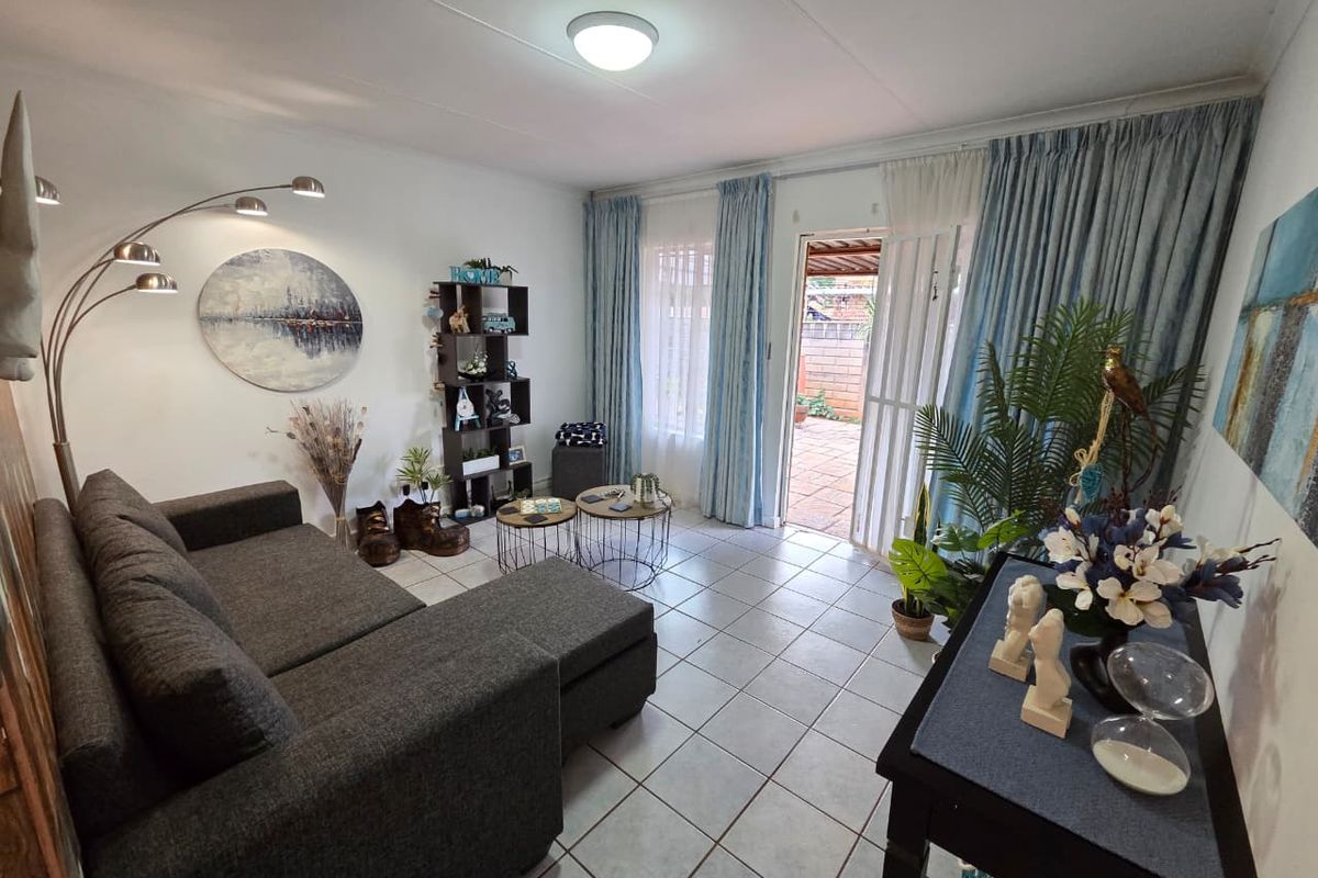 A bright living room featuring ceramic floor tiles and direct access to an outdoor patio area through a sliding door with a security gate.