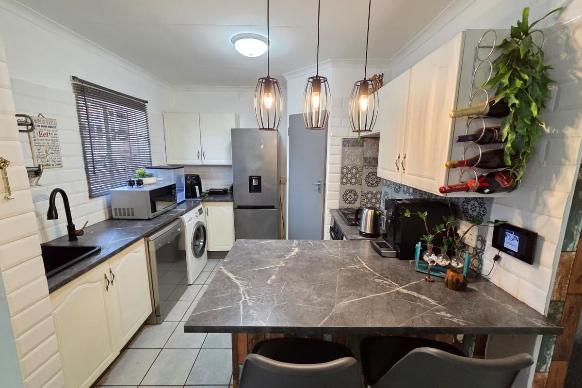 A functional kitchen featuring stone-look countertops, patterned tile backsplash, white cabinetry, and a breakfast bar area with modern pendant lighting.