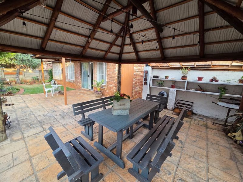Covered outdoor patio area featuring a thatched roof, exposed timber rafters, and built-in masonry shelving, providing a functional space for outdoor dining and relaxation.