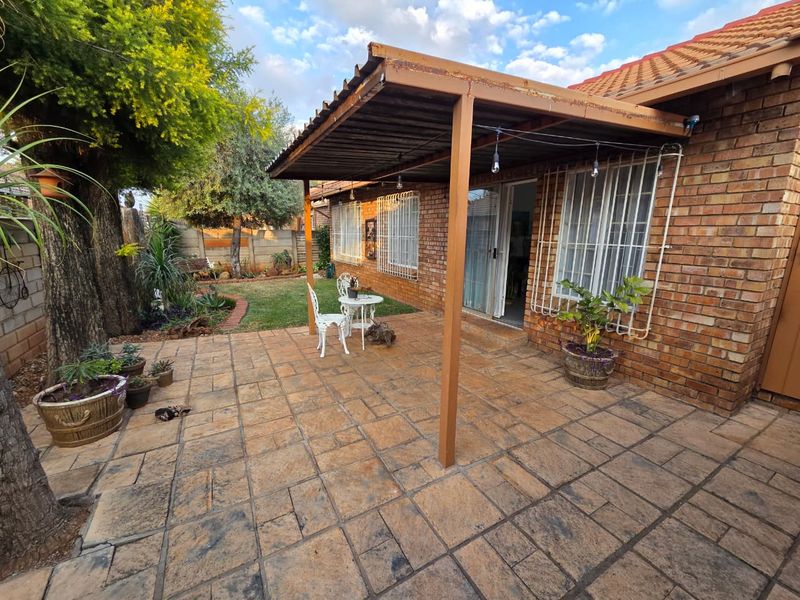 A covered brick patio area featuring tiled flooring and security bars on windows, providing a functional outdoor space for relaxation.