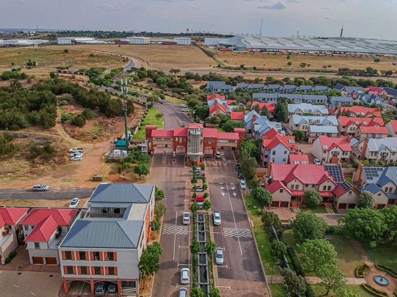 Aerial view of a residential estate featuring a gated security entrance, paved road network, and multiple detached homes with solar installations.
