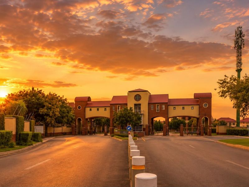 A scenic sunset view of the secure gated estate entrance, featuring architectural brickwork and controlled access points.