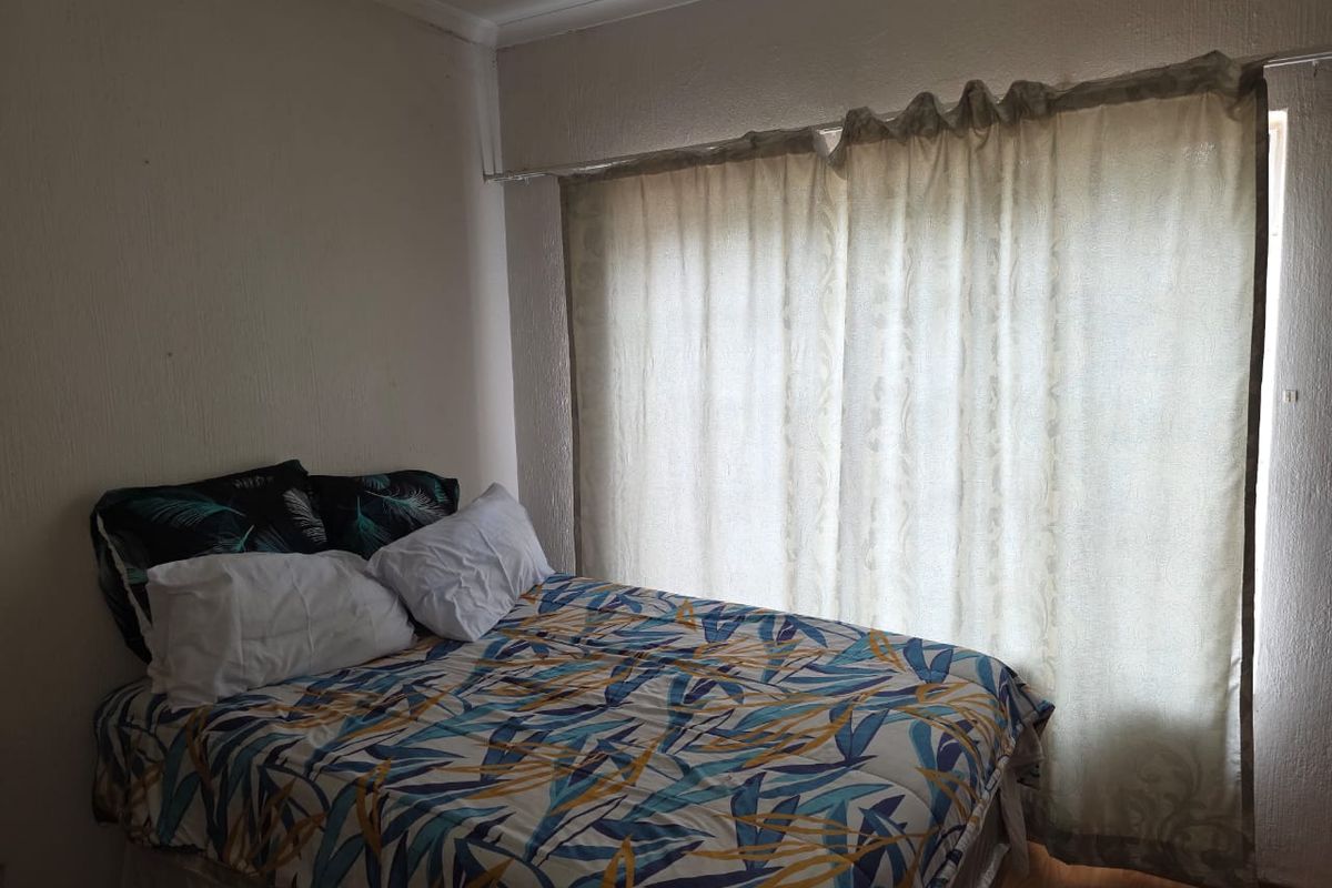 A bedroom featuring textured walls and large window coverage, providing natural light and a functional layout for a comfortable sleeping space.
