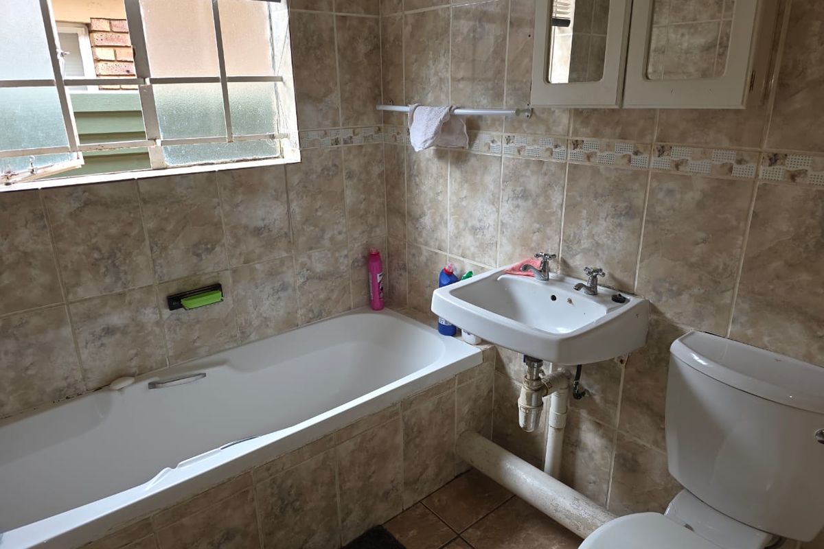 A functional bathroom featuring a built-in bathtub, wall-mounted basin, and toilet, finished with full-height ceramic wall tiling and a window for natural light.
