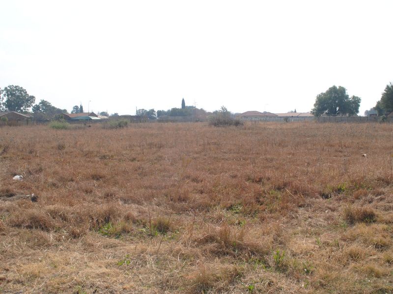 A wide-angle view of a vacant residential plot featuring dry grass and surrounding perimeter fencing in a suburban neighborhood.