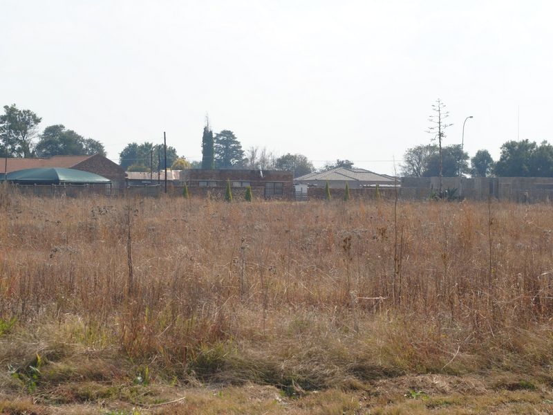 A view of a vacant residential plot featuring dry grass and surrounding perimeter walls, offering a blank canvas for future development.