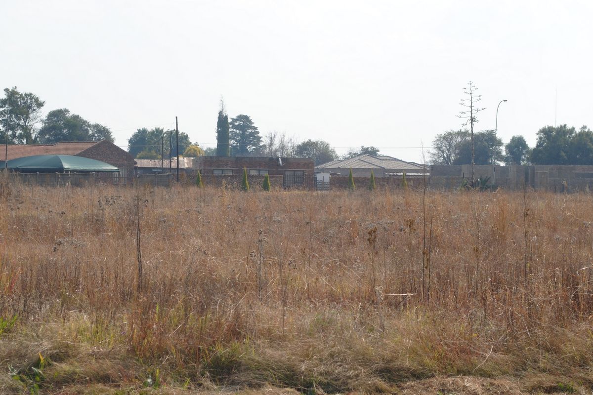 A view of a vacant residential plot featuring dry grass and surrounding perimeter walls, offering a blank canvas for future development.