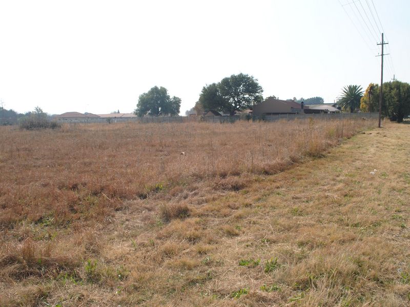 A vacant residential plot of land featuring dry grass, perimeter fencing, and an adjacent utility pole.