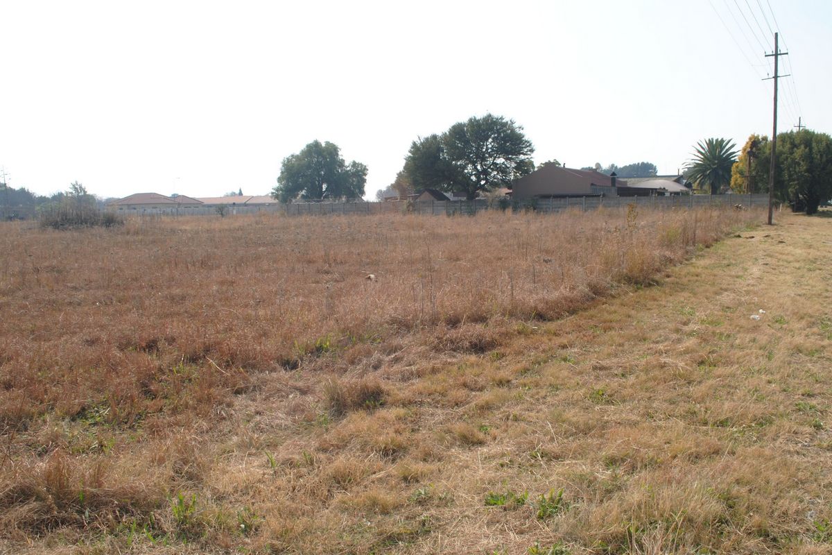A vacant residential plot of land featuring dry grass, perimeter fencing, and an adjacent utility pole.