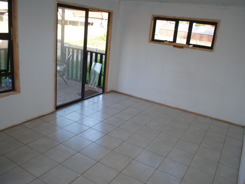 An empty, unfinished living room featuring tiled flooring, sliding glass doors leading to a deck, and large windows with aluminium frames.