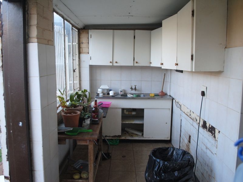 A functional scullery or utility area featuring built-in cabinetry, a stainless steel sink, and tiled finishes, currently requiring renovation and repair.