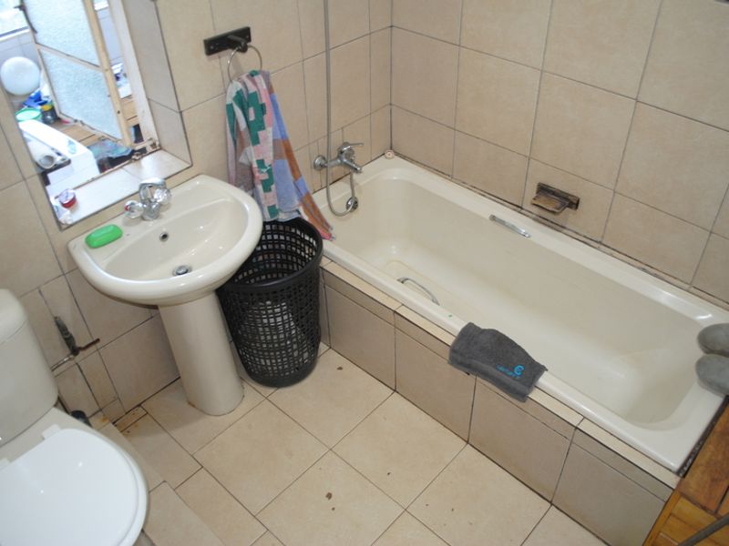 A functional bathroom featuring a pedestal basin, bathtub with shower mixer, and tiled finishes throughout, offering potential for modernization.