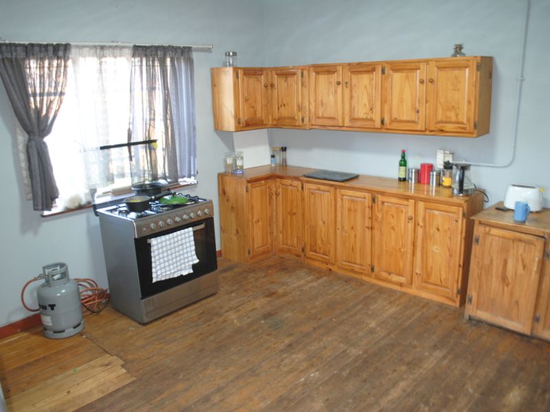 A functional kitchen featuring timber cabinetry, a gas stove, and original timber flooring, offering potential for modernization and aesthetic updates.