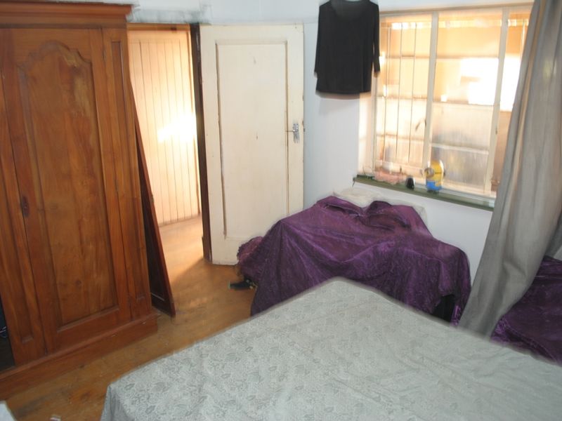 A bedroom featuring timber flooring, a window with security bars, and a traditional timber door, requiring cosmetic updates to improve its overall condition.