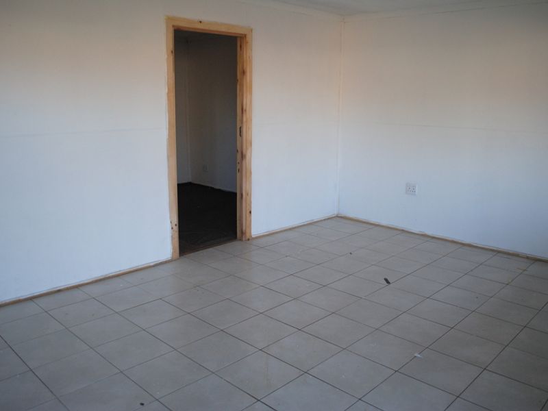 An empty bedroom featuring ceramic floor tiles and an unfinished wooden door frame, awaiting final touches and skirting boards.