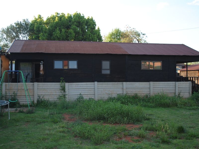 Rear view of a timber-clad dwelling featuring a corrugated metal roof and a precast concrete boundary wall set within a garden area.