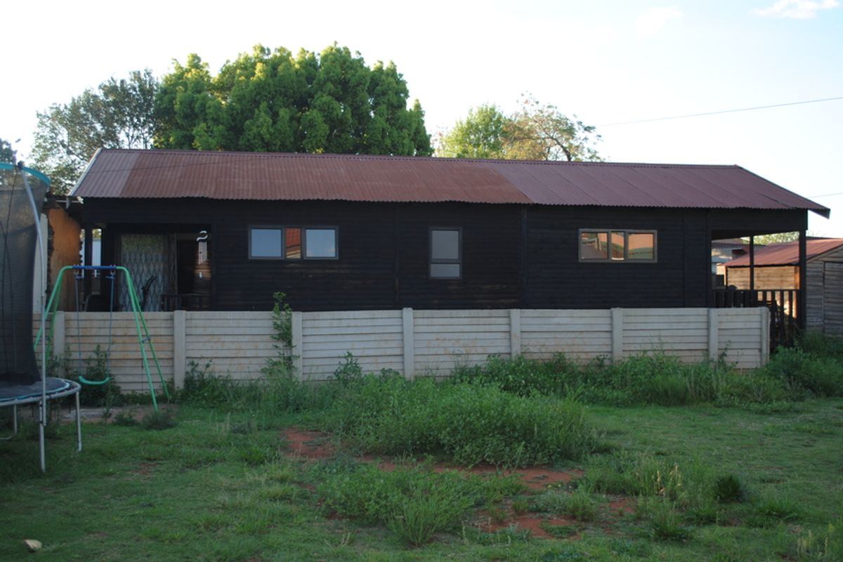 Rear view of a timber-clad dwelling featuring a corrugated metal roof and a precast concrete boundary wall set within a garden area.