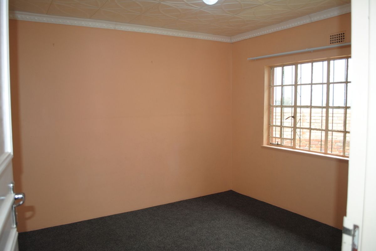 An empty bedroom featuring carpet flooring, a textured ceiling with cornice, and a window fitted with security bars.