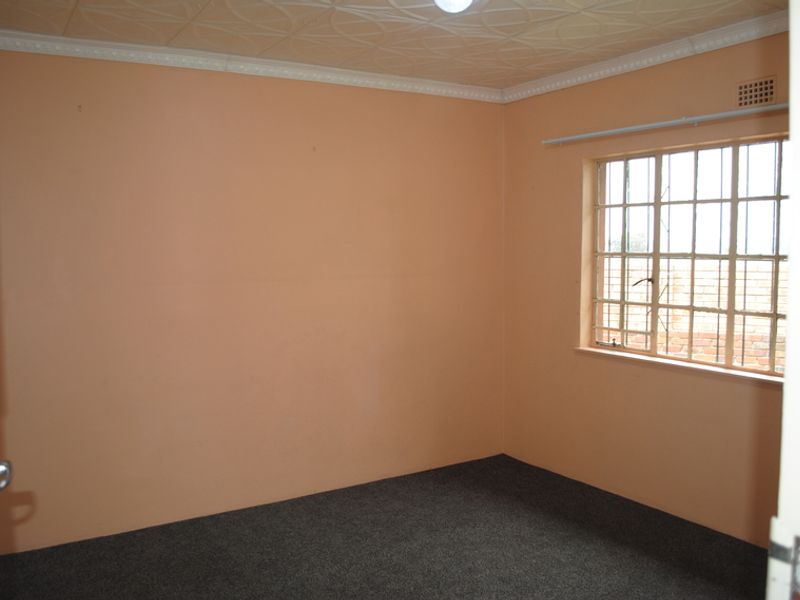 An empty bedroom featuring carpet flooring, a textured ceiling with cornice, and a window fitted with security bars.