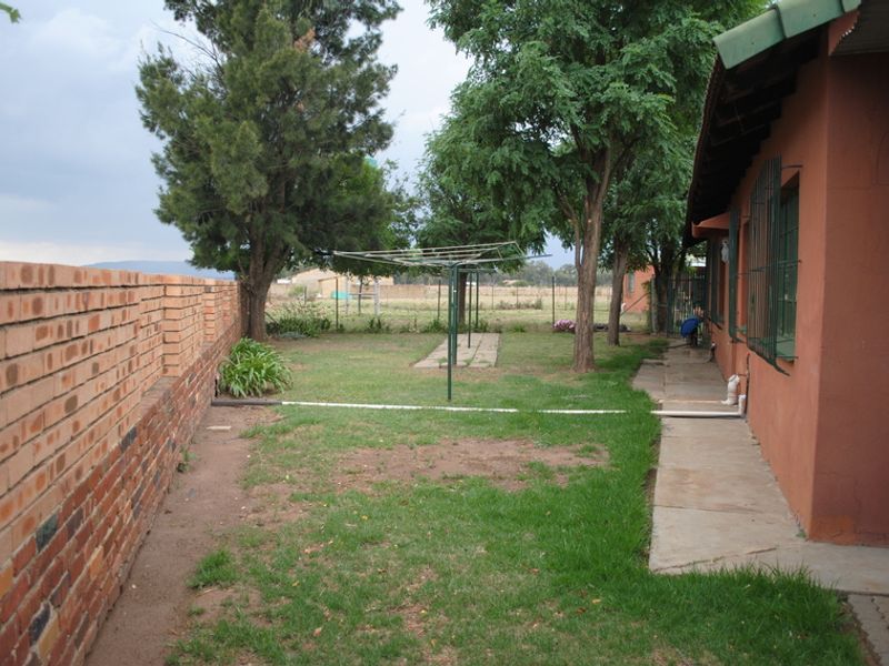 Rear garden area featuring a brick boundary wall, concrete pathway, and established trees, providing a functional outdoor space with potential for landscaping improvements.