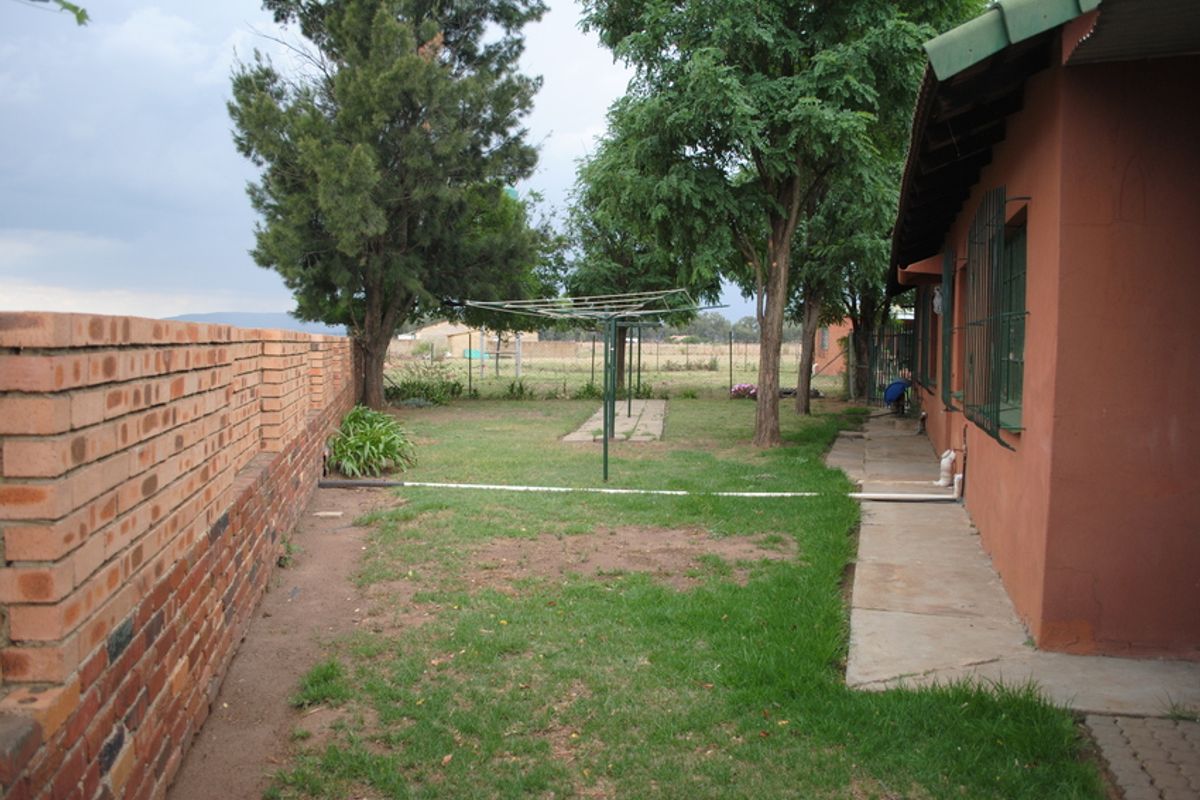 Rear garden area featuring a brick boundary wall, concrete pathway, and established trees, providing a functional outdoor space with potential for landscaping improvements.