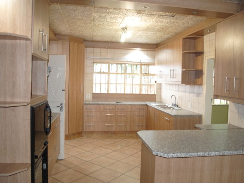 A functional kitchen featuring light wood-look cabinetry, laminate countertops, tiled flooring, and a built-in oven, offering a clean and practical workspace.