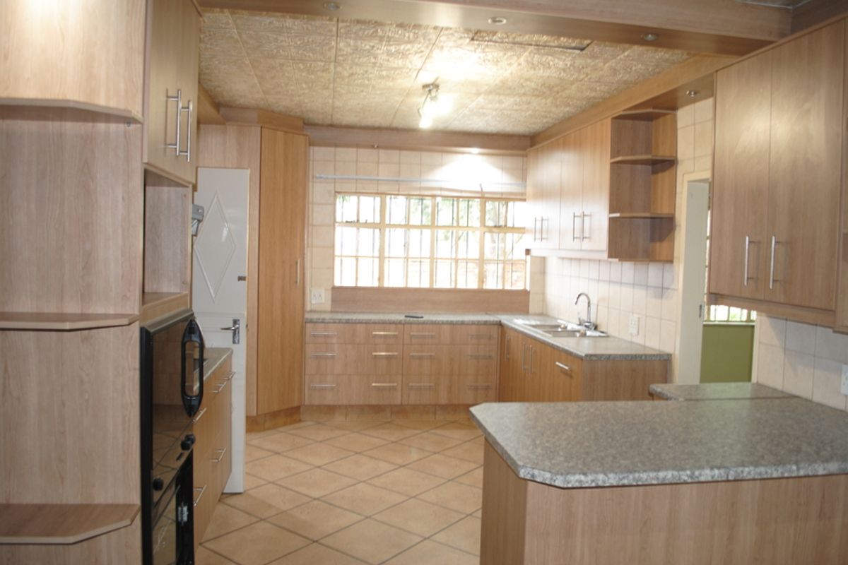 A functional kitchen featuring light wood-look cabinetry, laminate countertops, tiled flooring, and a built-in oven, offering a clean and practical workspace.