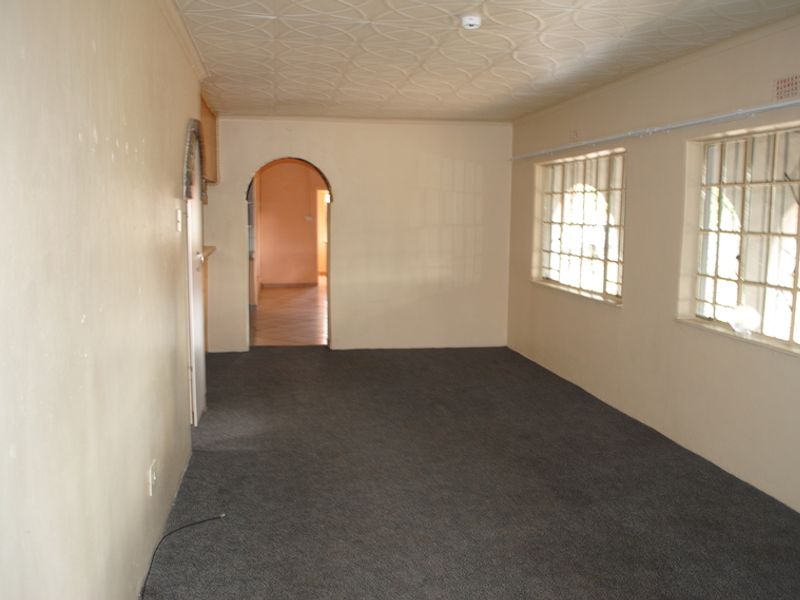 An empty living room featuring a patterned ceiling, arched doorway, and windows fitted with security bars.