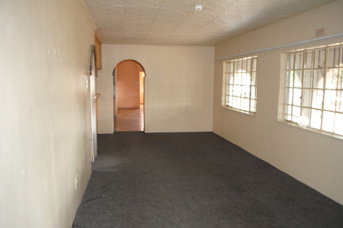 An empty living room featuring a patterned ceiling, arched doorway, and windows fitted with security bars.