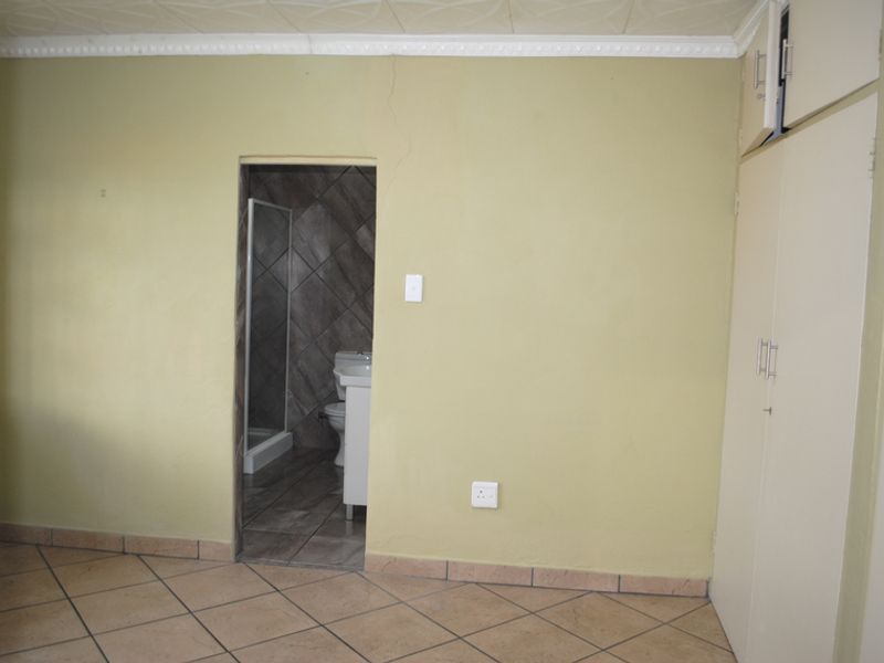 A bedroom featuring tiled flooring, built-in cupboards, and an en-suite bathroom access point, showing signs of wall cracking.