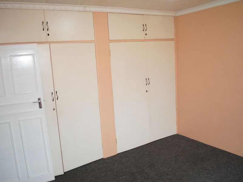 A vacant bedroom featuring built-in cupboards with overhead storage, carpeted flooring, and decorative ceiling cornicing.