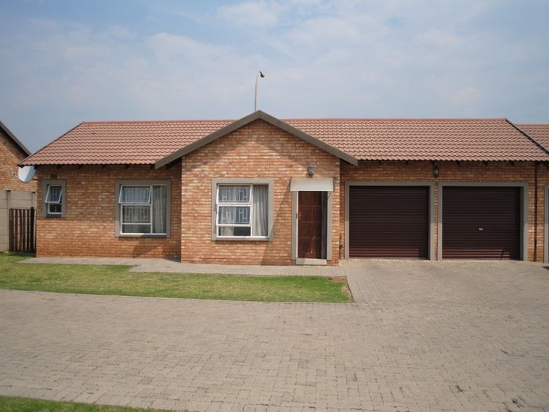 Front elevation of a face brick townhouse featuring a double garage with roller doors, paved driveway, and tiled roof.