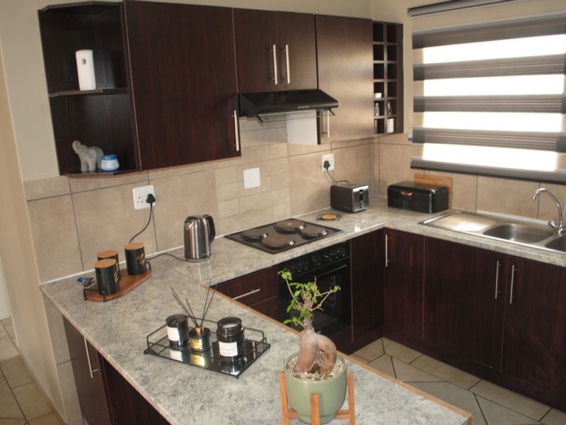 A functional kitchen featuring dark wood cabinetry, laminate countertops, built-in oven with electric hob, extractor fan, and a double sink with tiled backsplash.