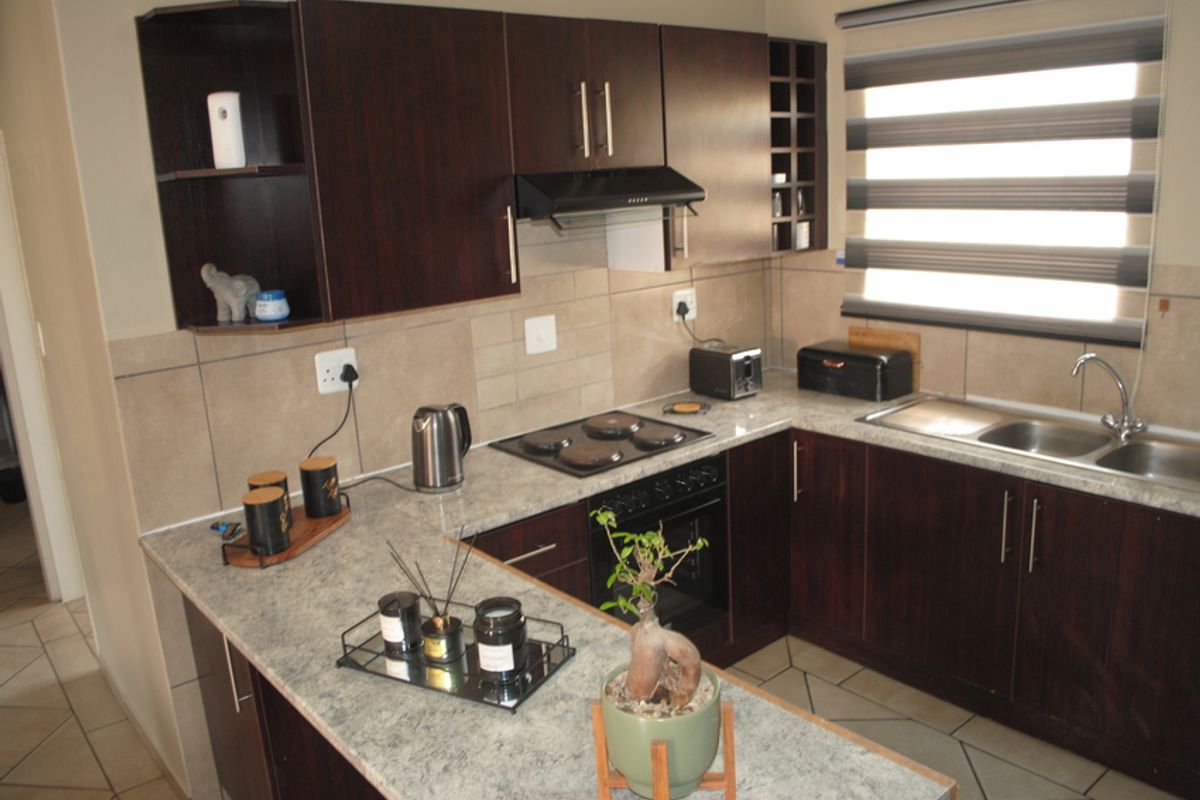 A functional kitchen featuring dark wood cabinetry, laminate countertops, built-in oven with electric hob, extractor fan, and a double sink with tiled backsplash.