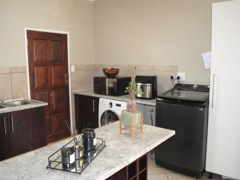 A functional laundry area featuring built-in cabinetry, laminate countertops, a stainless steel sink, and tiled finishes, providing practical utility space.