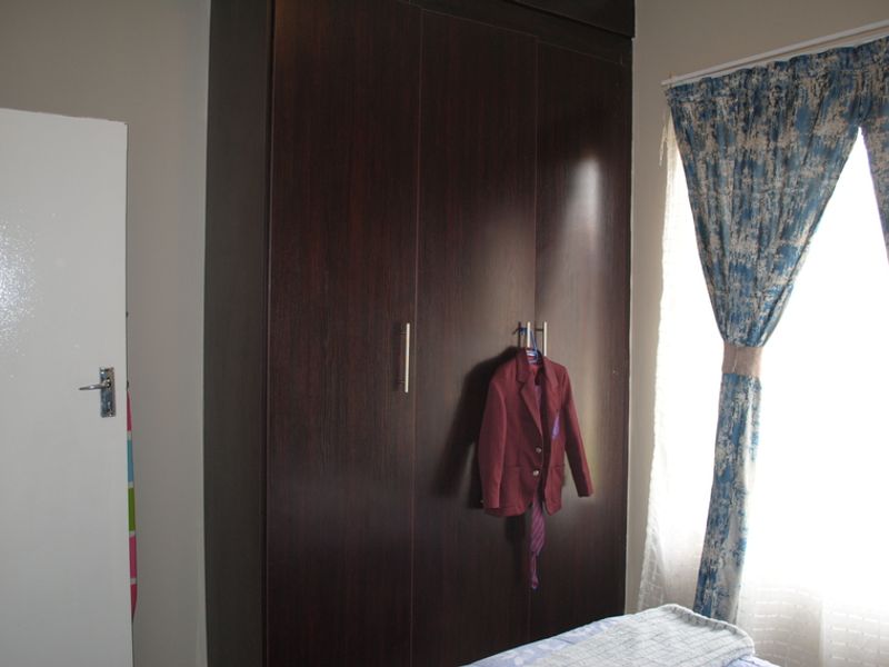 A bedroom featuring a dark wood built-in wardrobe and natural light from the window.