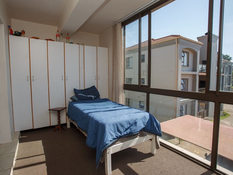 A bedroom featuring built-in cupboards and large windows that provide ample natural light and a view of the surrounding apartment complex.