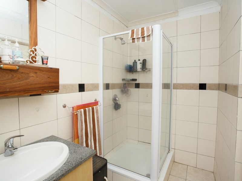 A functional bathroom featuring a corner shower enclosure, tiled walls with decorative accents, and a vanity basin with a stone-look countertop.