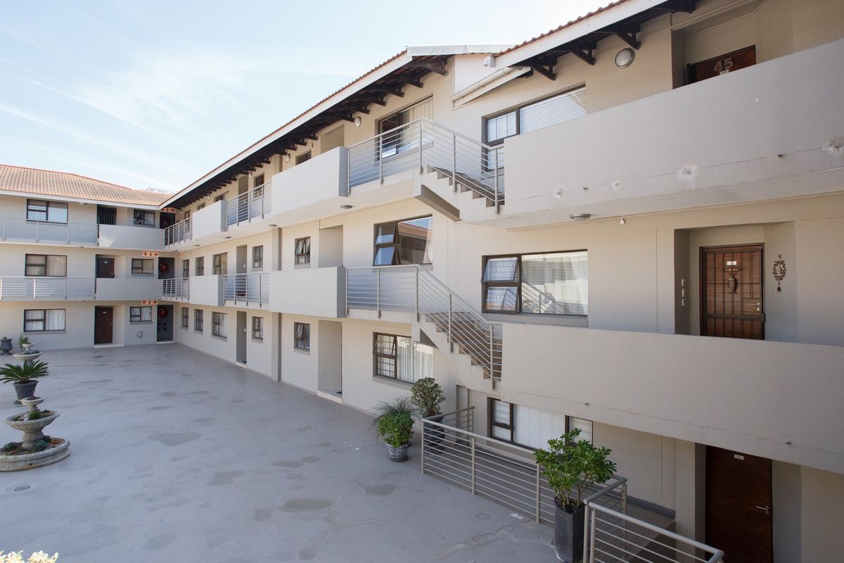 Exterior view of a multi-story apartment complex featuring a paved courtyard, external staircases, and secure unit entrances with tiled roofing.