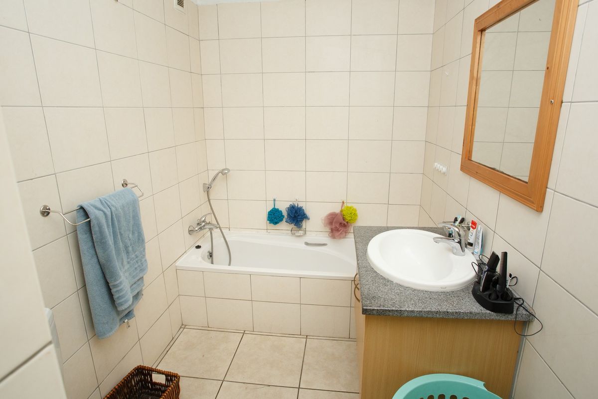 A functional bathroom featuring a built-in bathtub, vanity cabinet with basin, and full-height wall tiling. The space is dated and requires cosmetic updates.