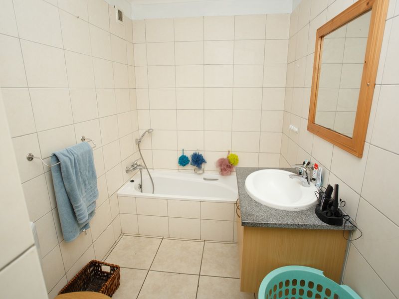A functional bathroom featuring a built-in bathtub, vanity cabinet with basin, and full-height wall tiling. The space is dated and requires cosmetic updates.