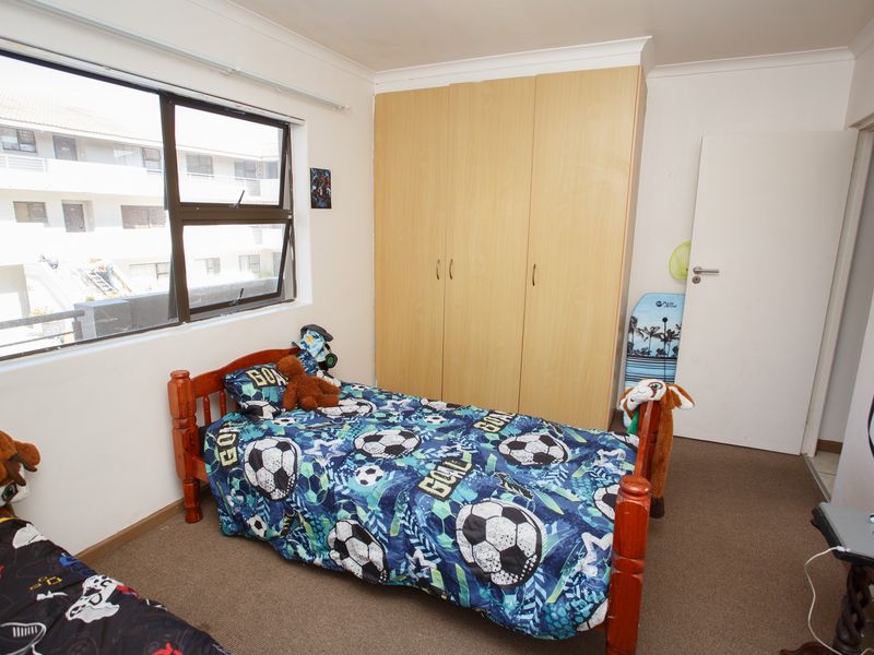 A functional bedroom featuring a built-in wardrobe, carpeted flooring, and a large window providing natural light.