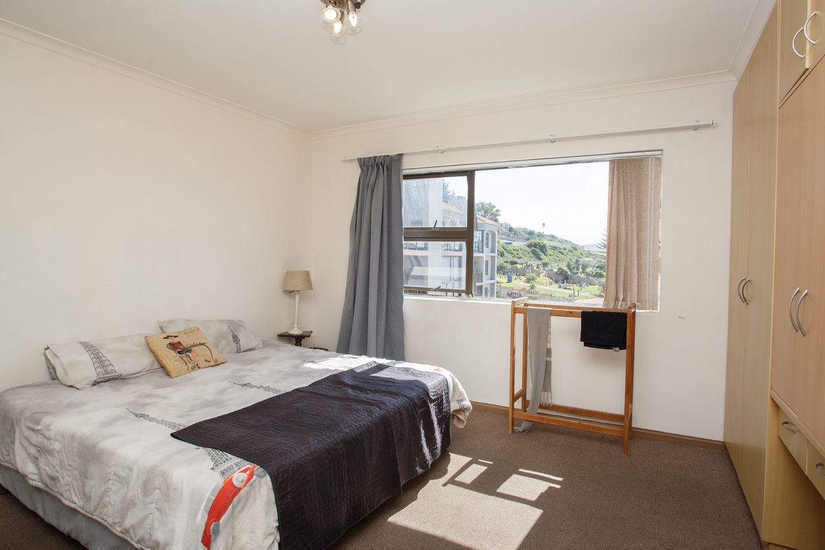 A functional bedroom featuring built-in cupboards, carpeted flooring, and a window with natural light and exterior views.