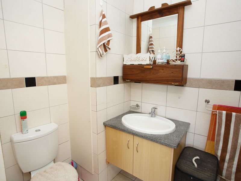 A functional bathroom featuring a vanity with a basin, wall-mounted storage, a mirror, and a toilet, finished with neutral wall tiling.