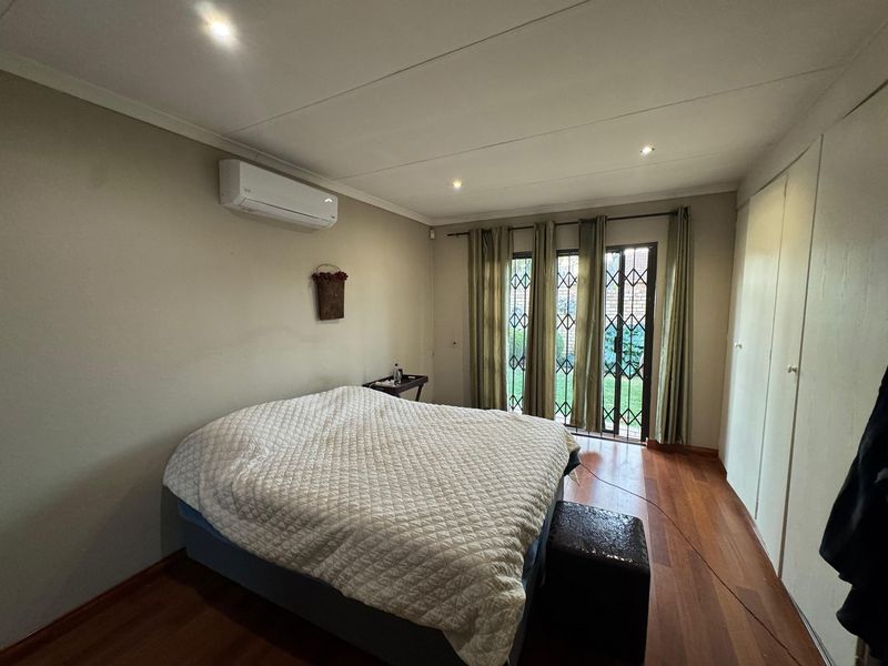 Spacious bedroom featuring laminate flooring, built-in cupboards, a split-system air conditioner, and direct access to the garden through a secure sliding glass door.