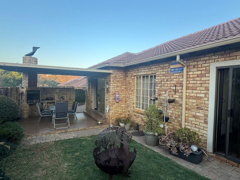 Rear exterior view of the townhouse featuring a brick facade, a covered patio with a built-in braai, and a small garden area.