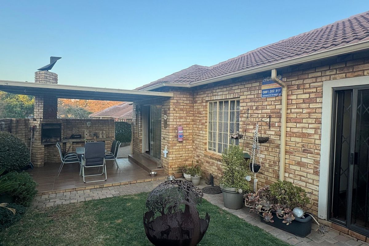 Rear exterior view of the townhouse featuring a brick facade, a covered patio with a built-in braai, and a small garden area.