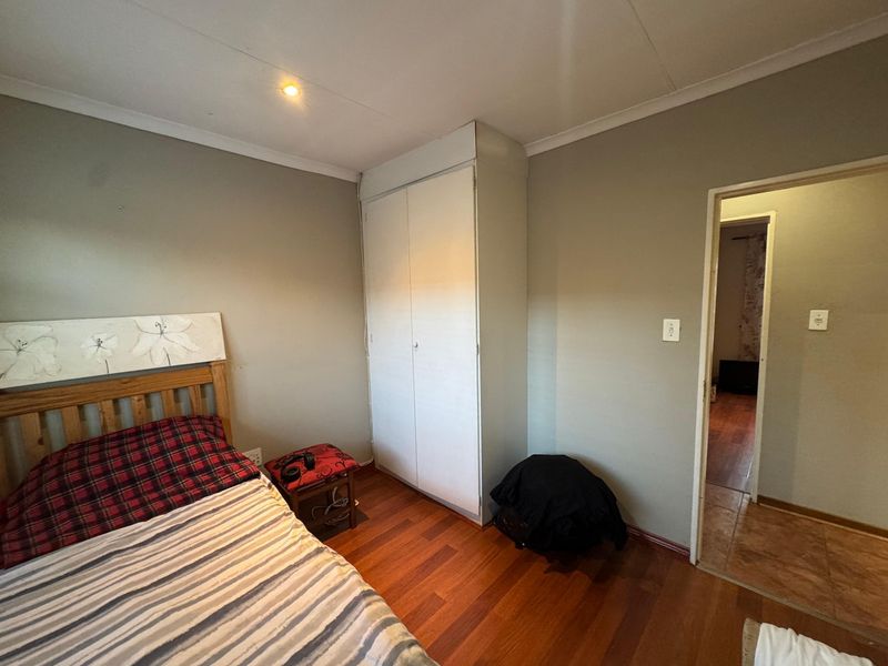 A bedroom featuring laminate flooring, a built-in wardrobe, and neutral wall finishes, providing a functional space with direct access to an adjacent room.
