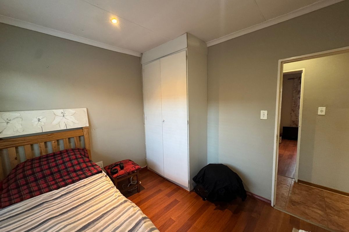 A bedroom featuring laminate flooring, a built-in wardrobe, and neutral wall finishes, providing a functional space with direct access to an adjacent room.